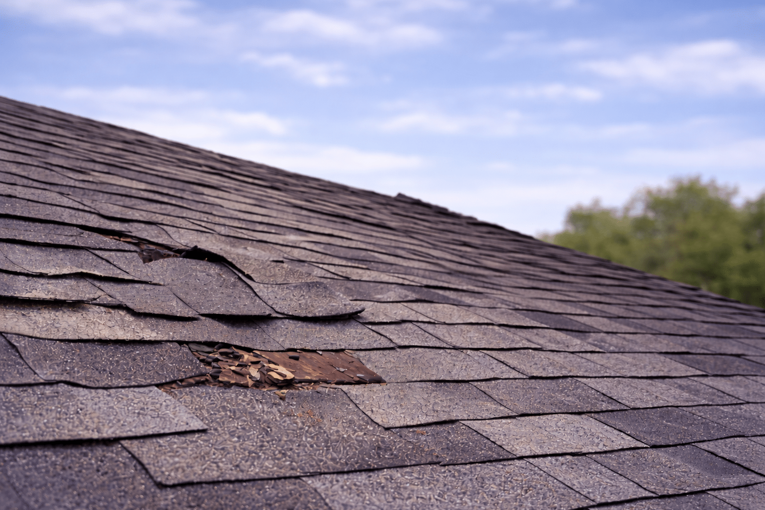 Damaged asphalt shingle roof with missing and curling shingles