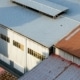 An aerial view of a large industrial warehouse facility with corrugated metal roofing panels in shades of grey and brown.