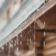 Detailed view of a blue-gloved hand placing a single grey square paver stone into position within a larger paved area.