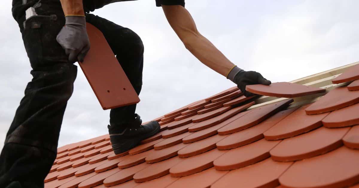 A roofer installing new terracotta clay tiles onto a residential roof structure.