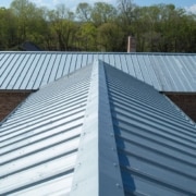 A top-down, aerial photograph taken from the perspective of a roofer. The image focuses on a newly installed light blue, vertically-ridged metal roof structure, highlighting the clean alignment and fastening patterns essential for a successful metal roof installation.