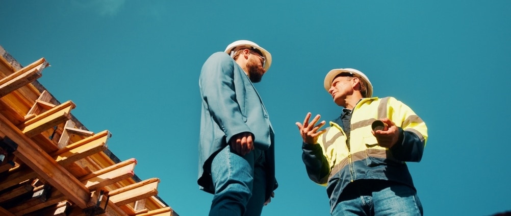 How to Spot a Storm-Chasing Roofing Scam in South Florida – two roofing professionals discussing a construction project beside a residential roof structure.
